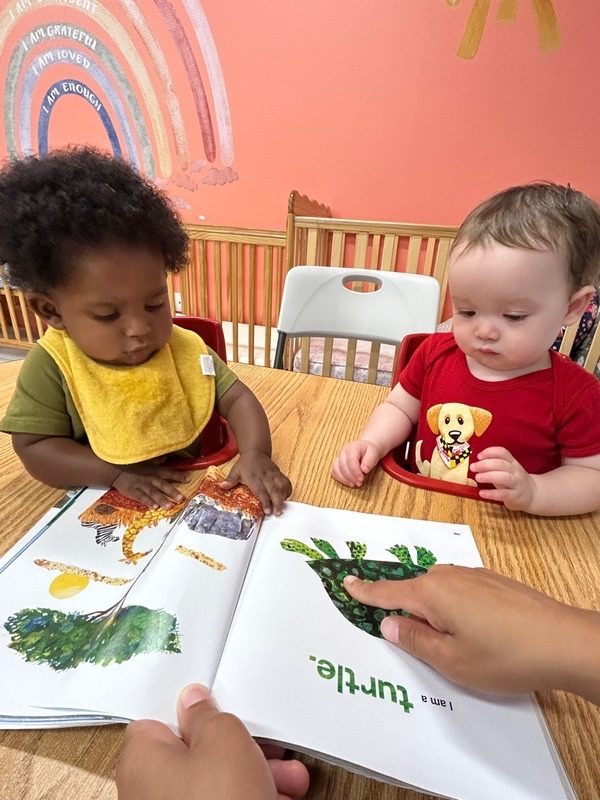 Two babies looking at a picture book with a teacher