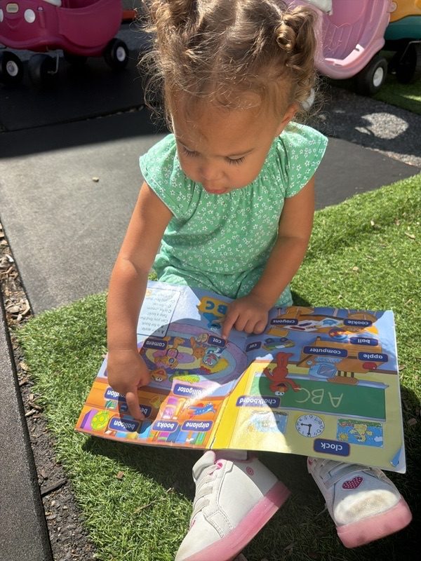 Toddler reading an ABC book outside on the playground turf