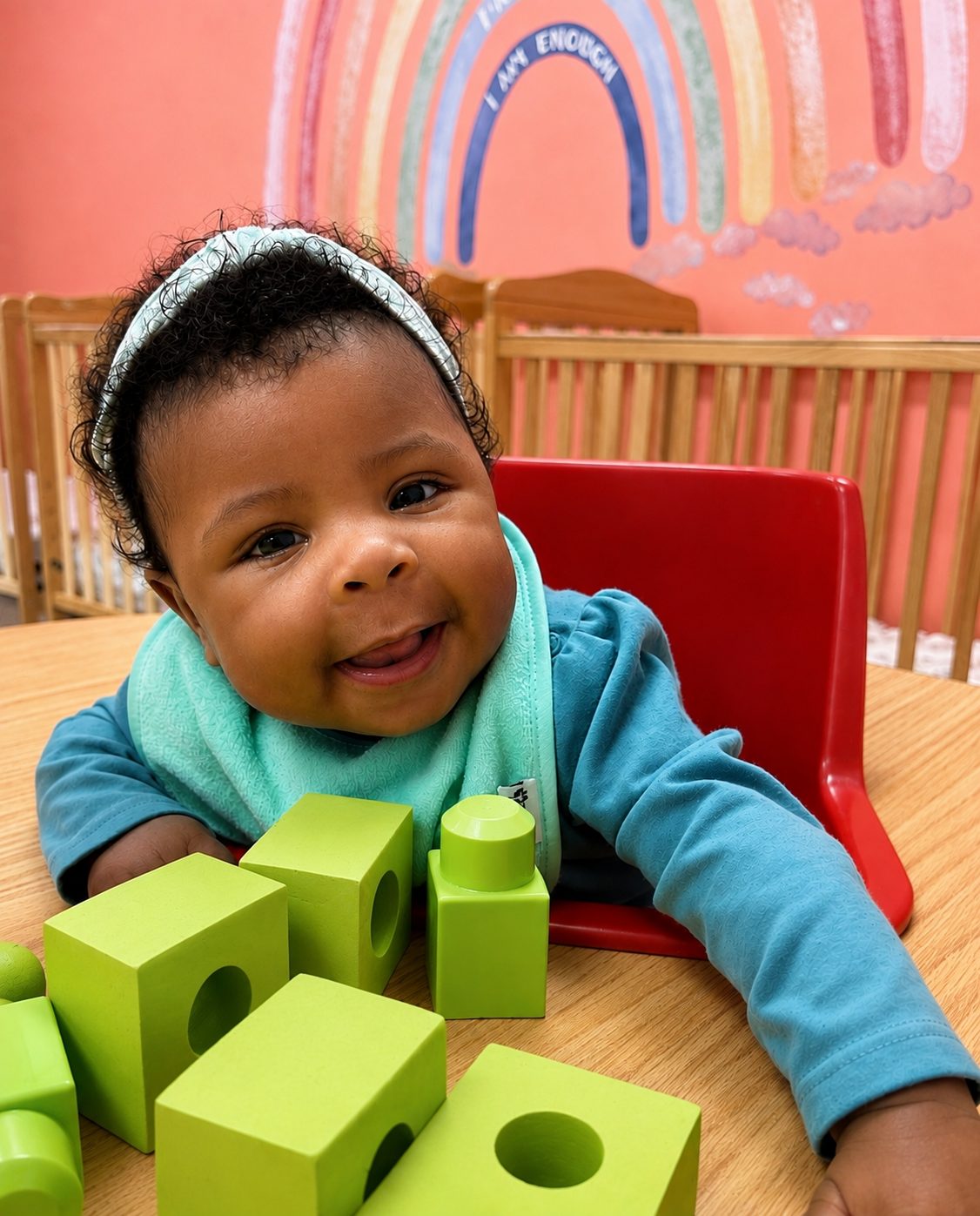 Smiling infant playing with green blocks in the infant room